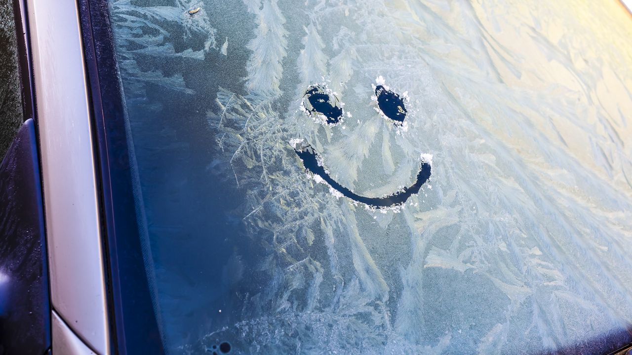 A smiley face is drawn in the ice on a car&#039;s window.