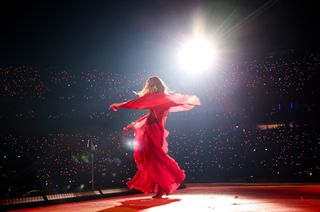 Taylor Swift dancing onstage at the eras tour wearing a red alberta ferretti dress with a semi sheer cape