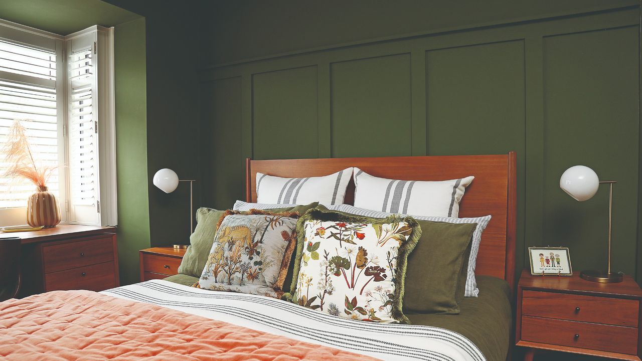 A colour-drenched green bedroom with shaker-style wall panelling behind the bed