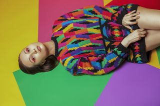 A model wearing a multicoloured patterned jumper, led on a geometric multicoloured background.