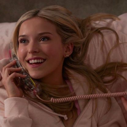 lexi minetree as elle woods talking on the phone wearing pink and lying in a pink bed in a still from the legally blonde prequel elle