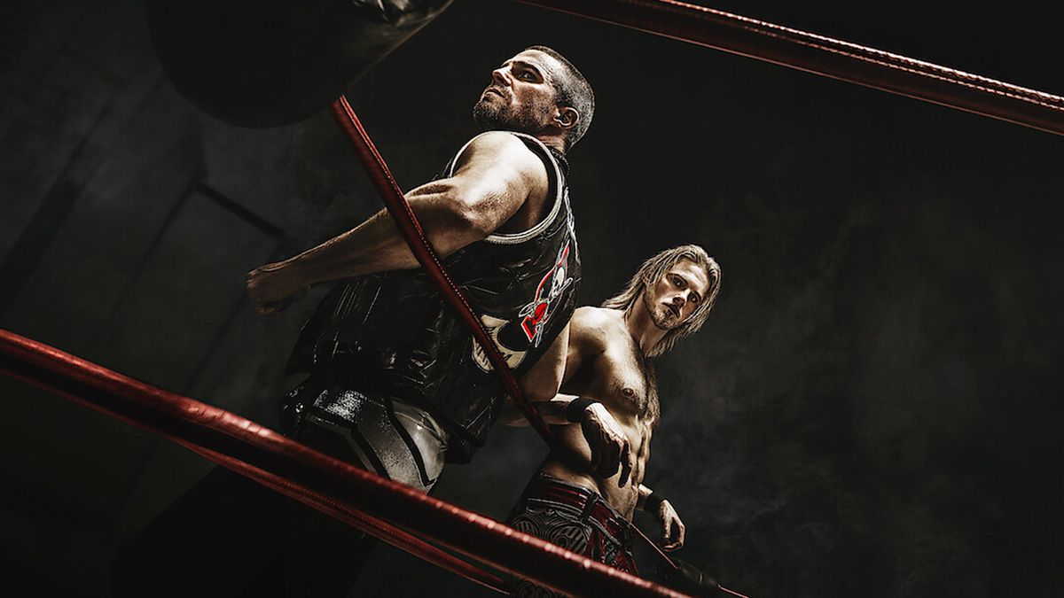 Two men stand in a wrestling ring posing