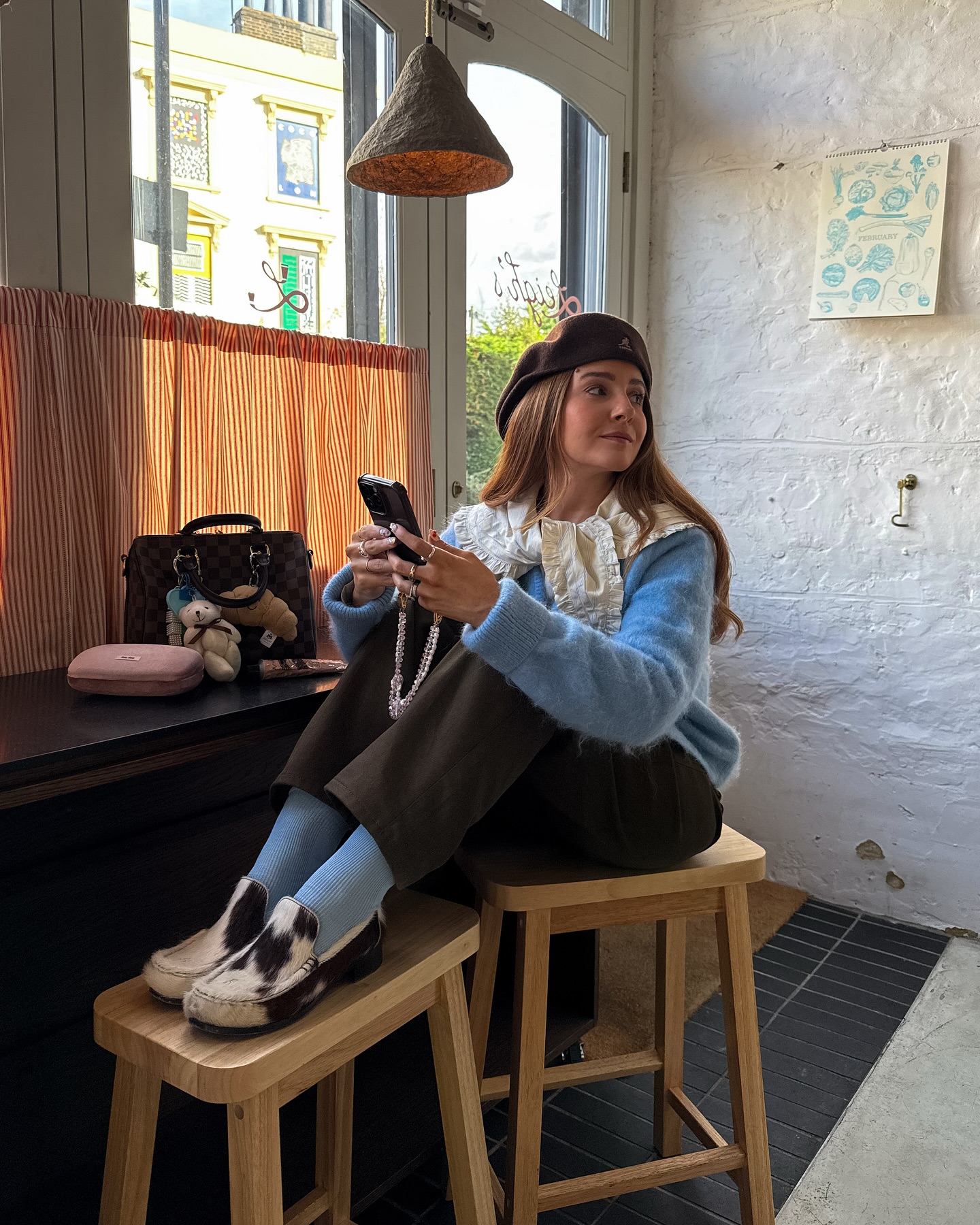 Girl sat on stool wearing cow print loafers on phone