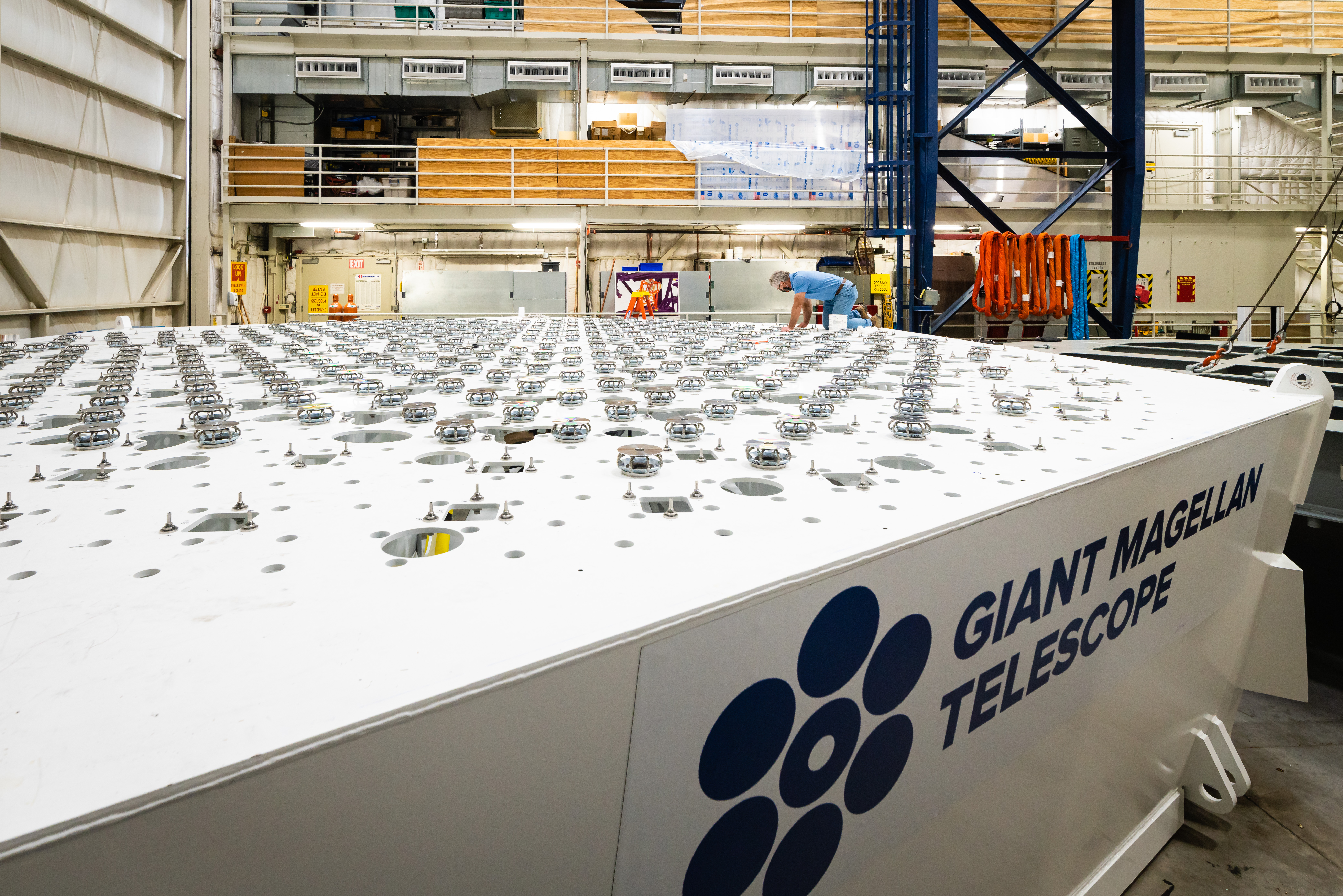 The Giant Magellan Telescope test cell is being outfitted with mirror supports and actuators in the Richard F. Caris Mirror Lab at the University of Arizona in Tucson. Kurt Kenagy inspects the static support hardware prior to attaching the mirror simulator (not shown).