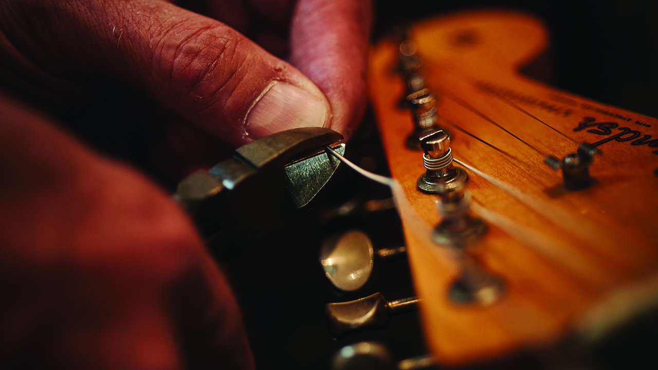 Closeup of hands changing guitar strings on a Fender Stratocaster