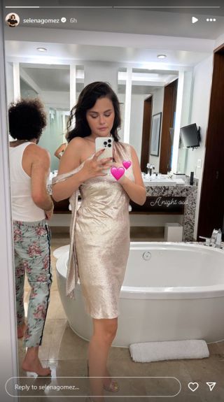 Selena Gomez taking a mirror selfie that features a pink heart emoji covering her left hand.