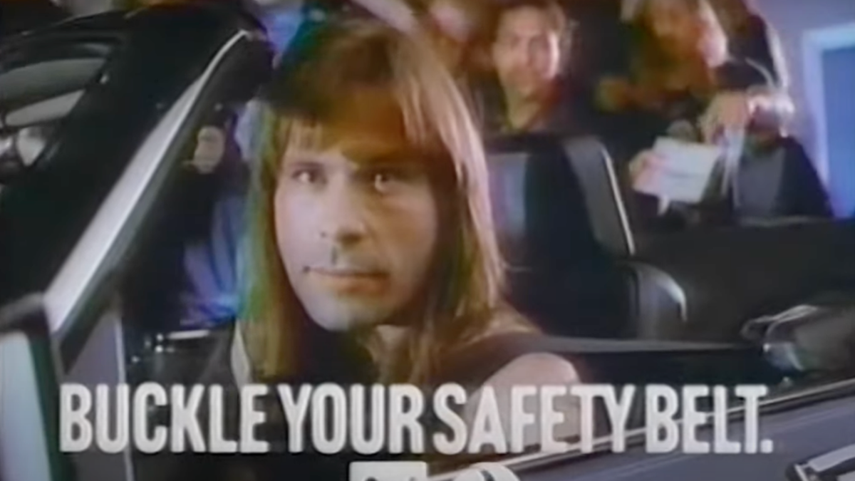 Iron Maiden singer Bruce Dickinson sat in a convertible and looking at the camera, with text reading &quot;Buckle your safety belt.&quot;