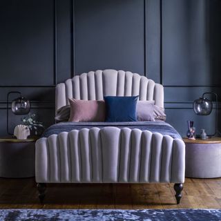 best colour combinations, indigo blue walls with lilac upholstered bed, blue, pink and lilac cushions, blue rug, side table, glass table lamp, wood flooring