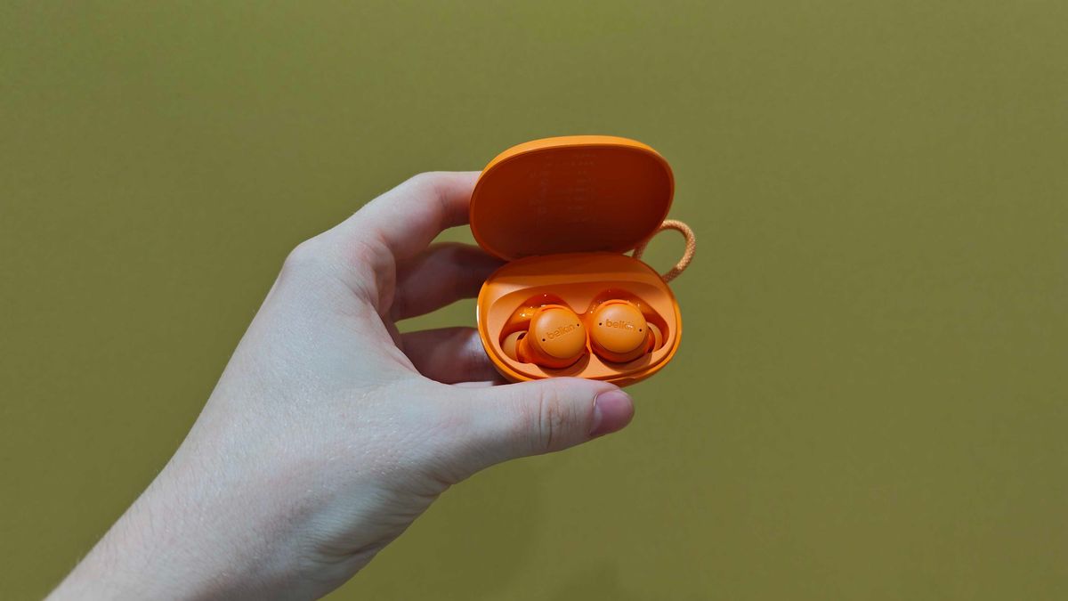 Belkin SoundForm Isolate Buds in orange and in a man's hand, with a wooden table in the background