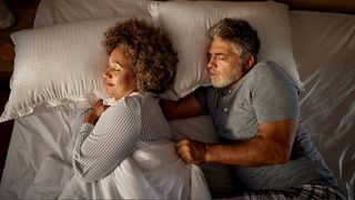 A man and woman in bed with the man trying to pull covers from woman.