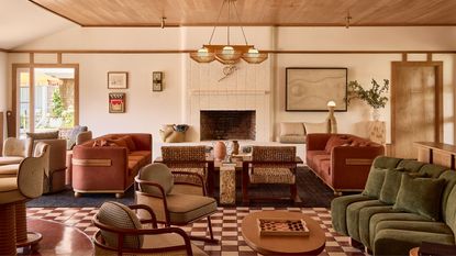 A spacious, earth-toned lounge with terracotta floor tiles, woven wicker chairs, a white brick fireplace, and a large wood-paneled ceiling