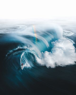 A surfer in a barrel wave with a rainbow