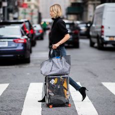 A woman pulls her suitcase and bag along a pedestrian crossing