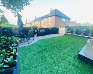 a backyard with artificial grass, with outdoor seating in the form of a black dining set, to the left