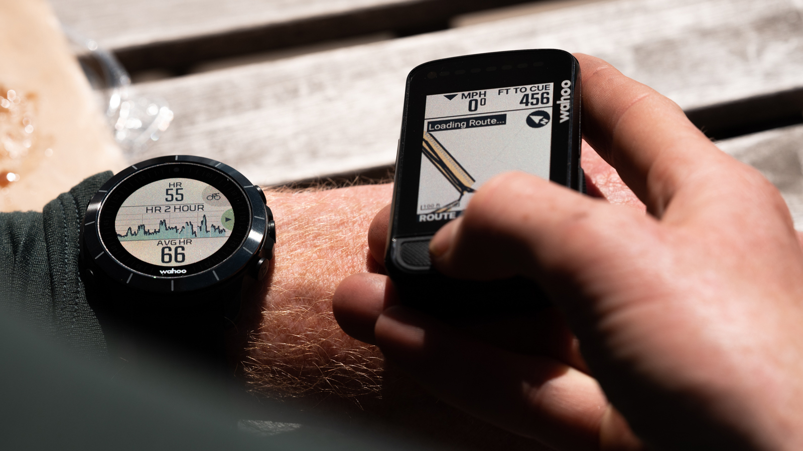 Someone wearing a Wahoo Elemnt Rival watch holds an Elemnt Bolt computer nearby, indicating the syncing of data between the two