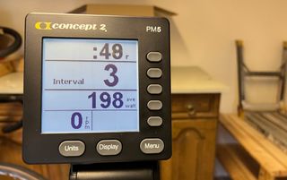 The Concept2 BikeErg PM5 monitor is enlarged and is showing a clear interval session with four metrics on display, time, interval number, average Watts and RPM