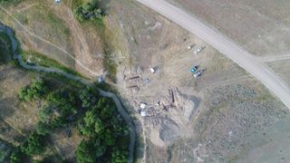 An aerial view of archaeological site with green trees and light colored soil.
