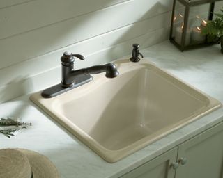 kohler river falls cast iron utility laundry sink mounted in a marble countertop with cream cabinetry