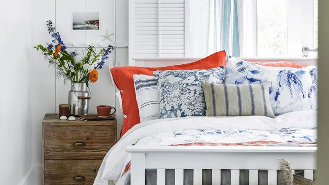 A bedroom with a white wooden bedframe and orange and blue bedding