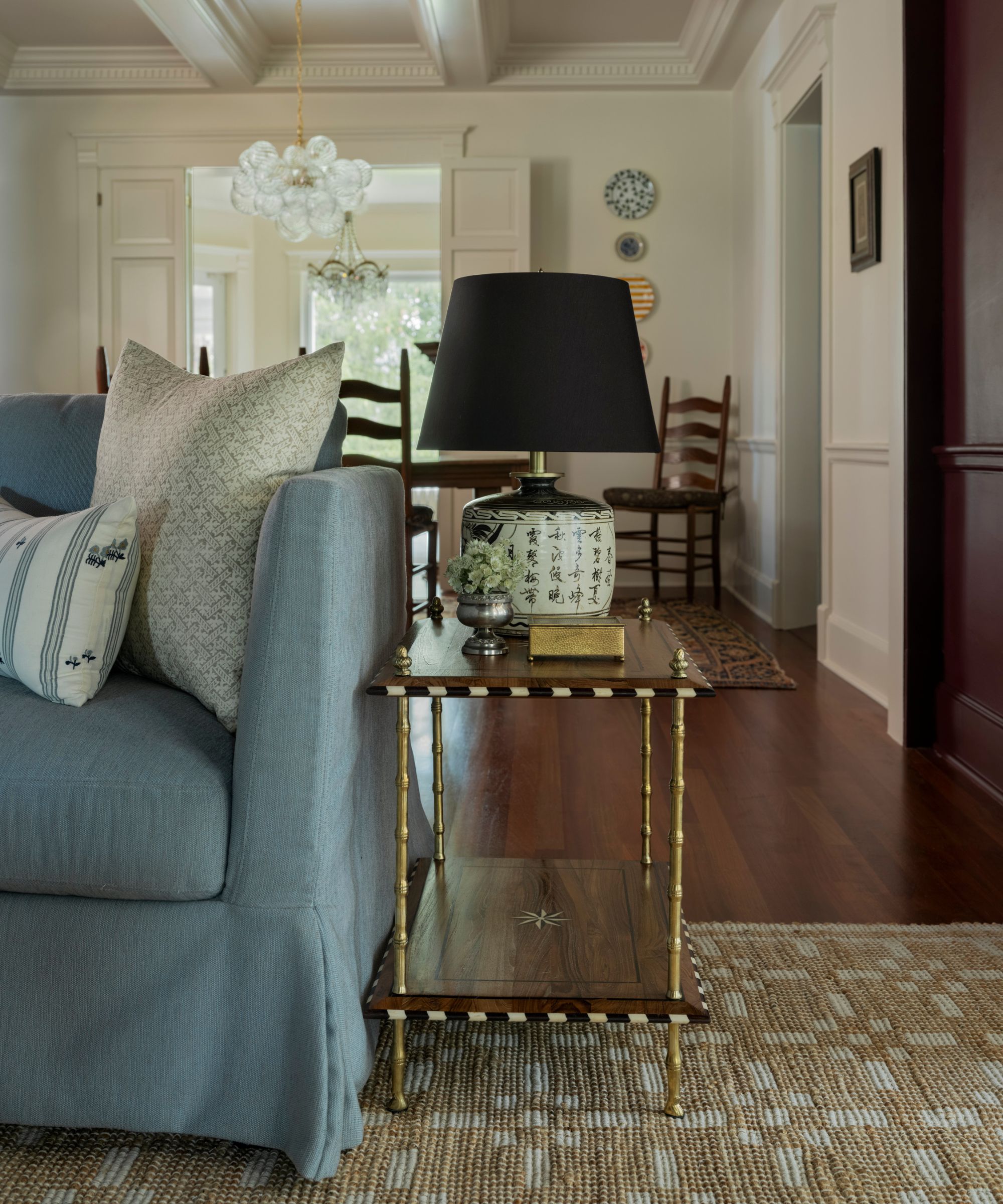 neutral living room with traditional ceiling molding and paneled walls with dark wood floors, a jute rug and a soft blue linen sofa