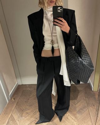 @hoskelsa wearing black blazer, black trousers, and black woven bag.