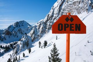 An orange "open" sign at a ski resort opening up to off-piste backcountry