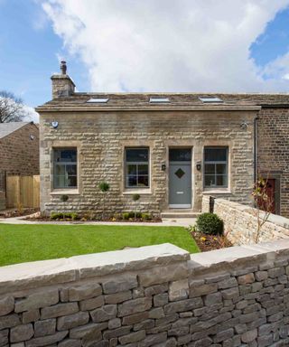 A traditional-style, one-storey stone property with blue RIBO windows from VELFAC, and a matching front door. A neat lawned garden, stone wall and borders sit in front of the property.