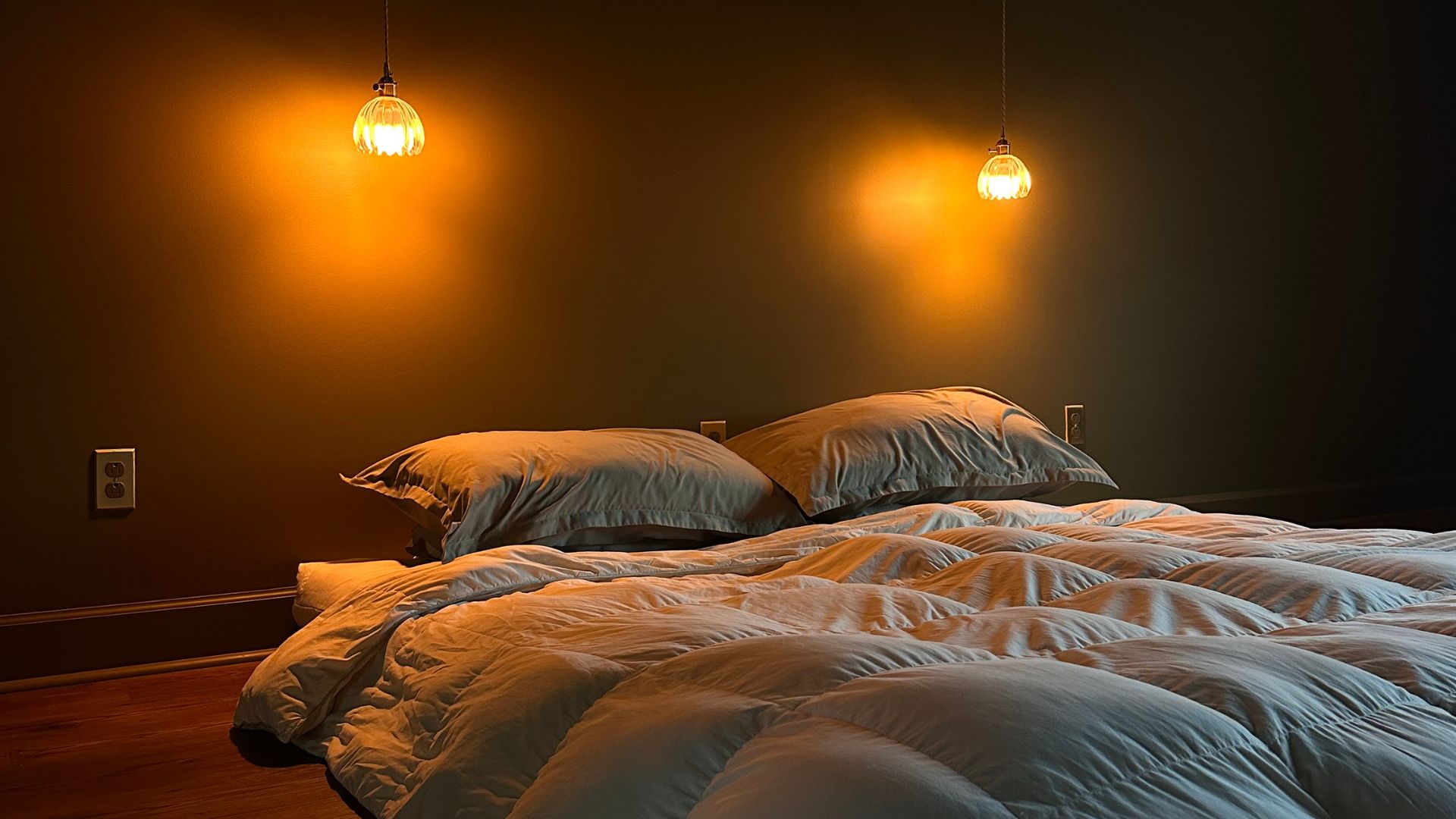A dark green room with hanging wall sconces over a Japanese floor mattress with blue bedding