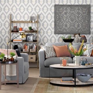 patterned wall paper living room with a wooden book shelf and grey sofas with color patterned pillows and a circle shaped coffee table