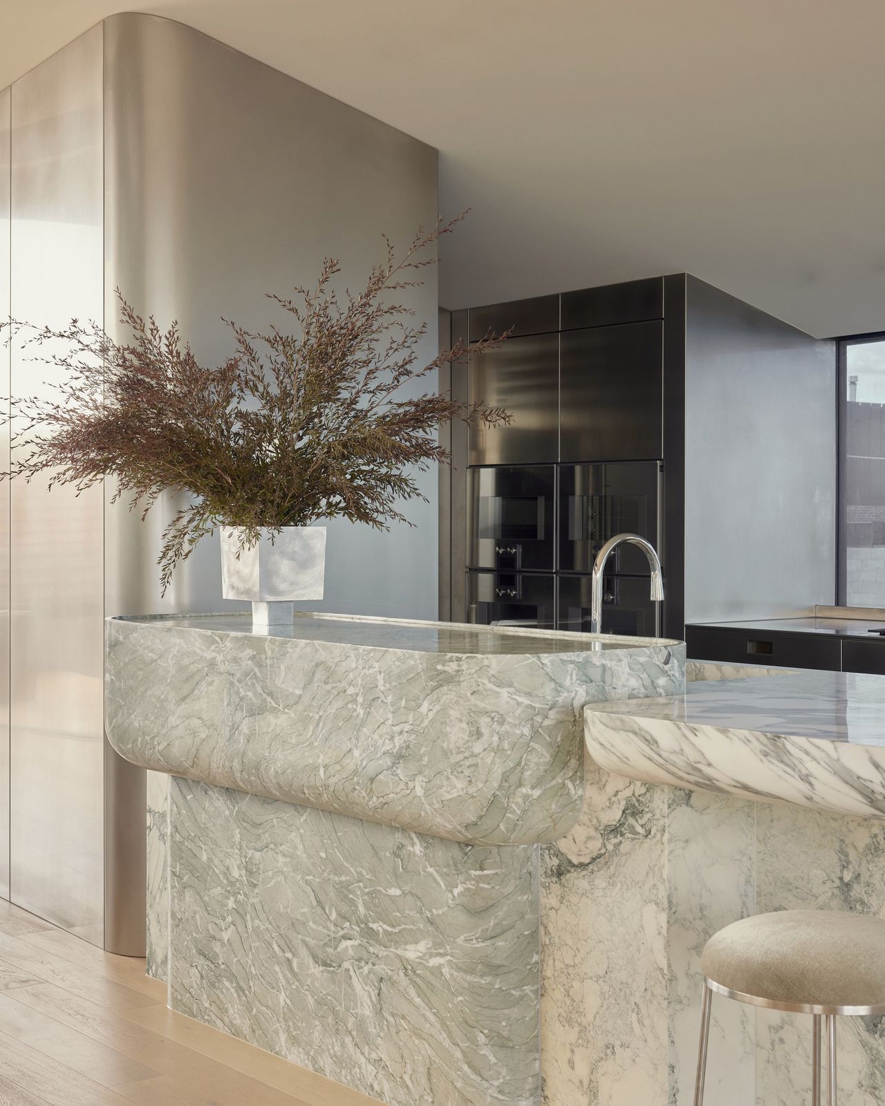 modern kitchen with curved stone island bench and stainless steel joinery with vase filled with foliage
