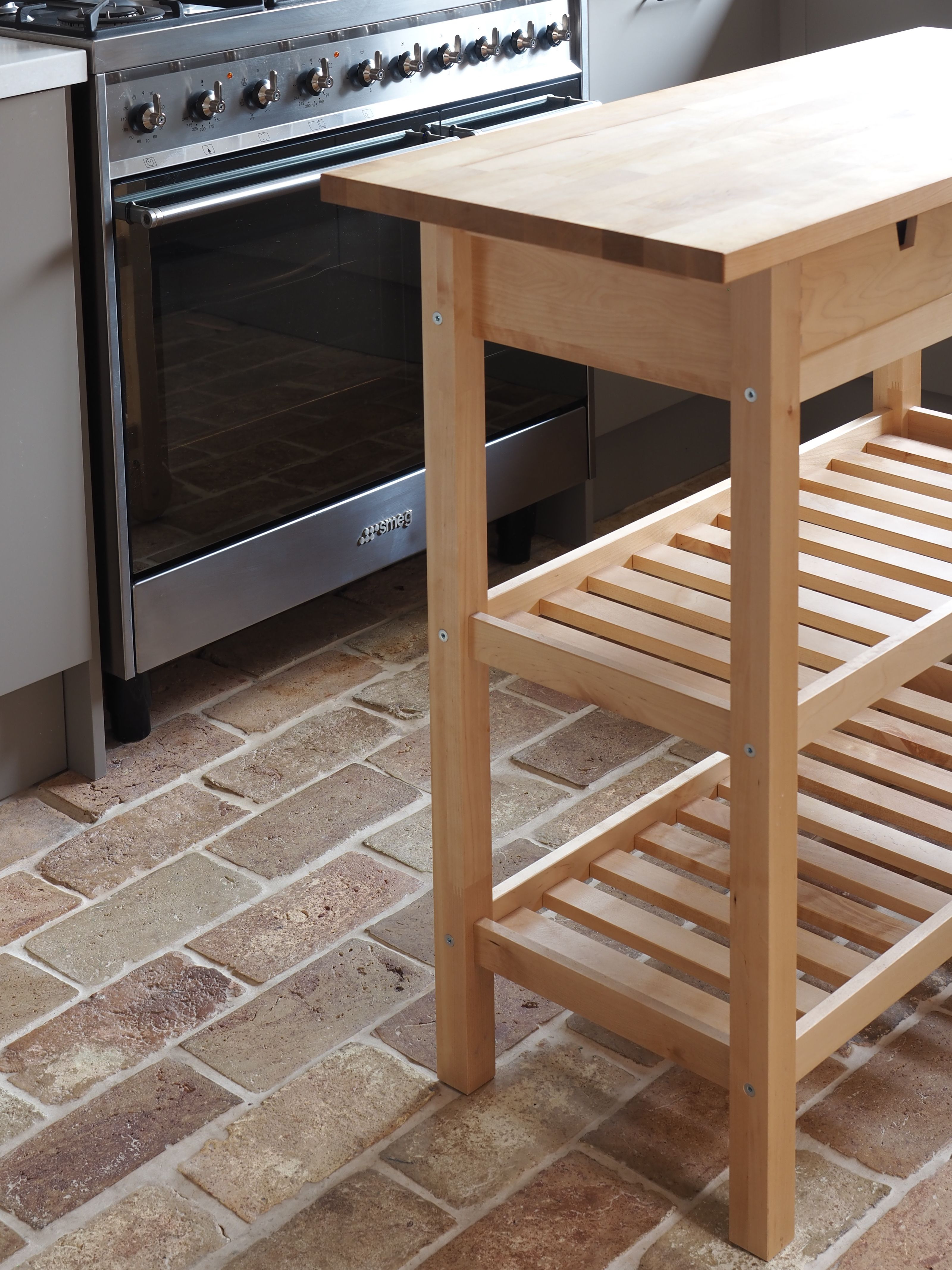 a small ikea kitchen island in a kitchen with a brick floor and an oven in the background