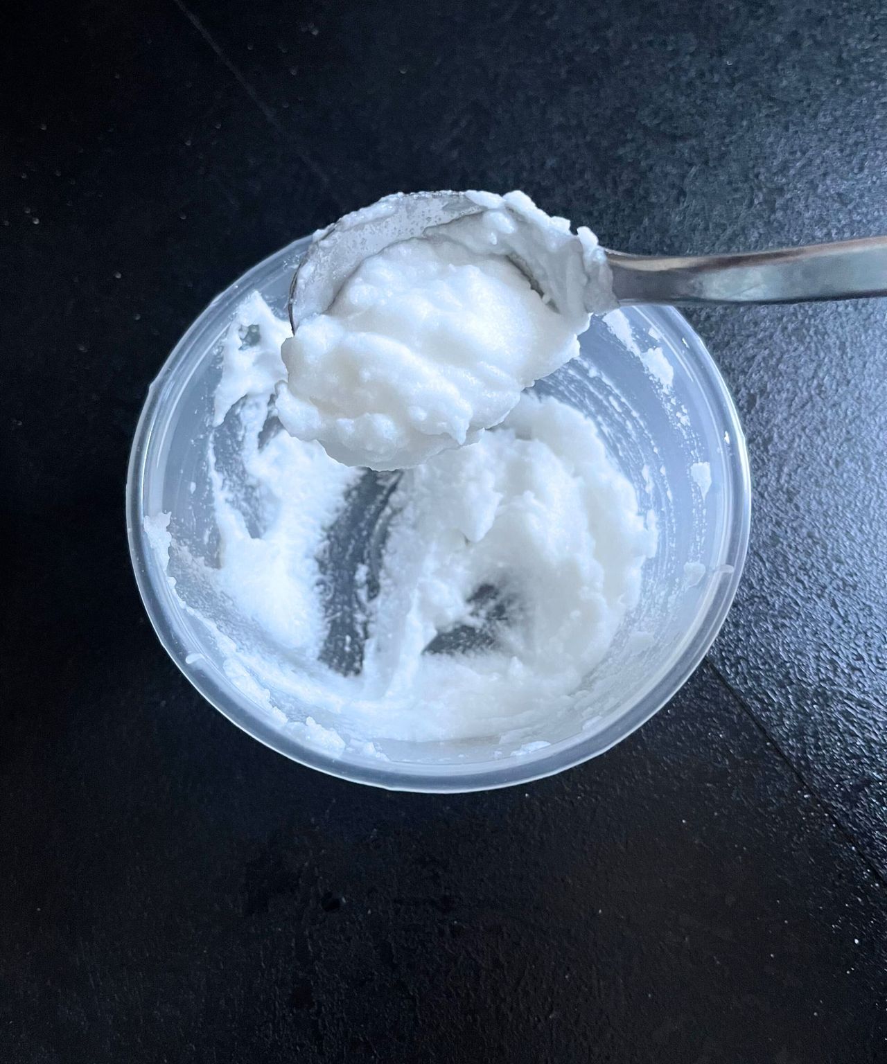 A baking soda paste in a round plastic container, sliding off a metal teaspoon