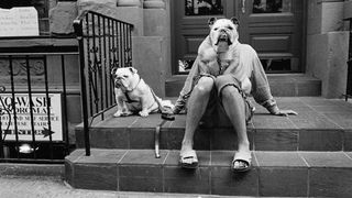 Black-and-white photo of two dogs on a doorstep, with one sitting on a person's lap