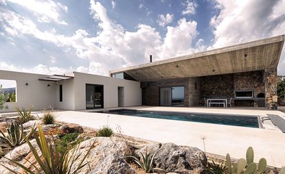A summer retreat in Greece. Outdoor area with a pool and a patio with gray metal seating and a grill, built into the stone wall.