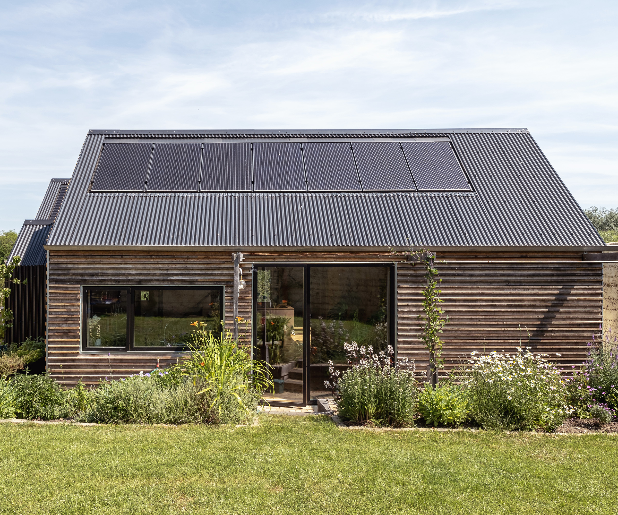 A small self build with solar panels and sliding glass doors with a lawn in front