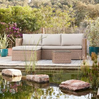 A rattan outdoor corner sofa by the side of a water feature