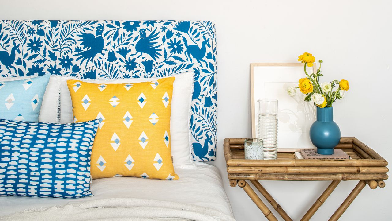 guest room ideas Blue patterned upholstered headboard with patterned yellow and blue tone scatter pillows, and bamboo bedside with yellow flower posy and water carafe.