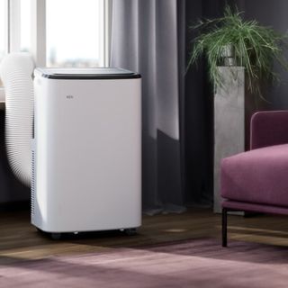 White portable air conditioner next to house plant and purple couch