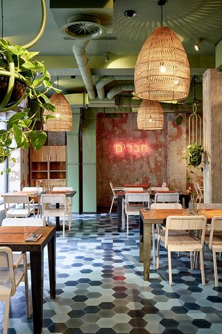 Restaurant with tables, chairs, patterned coloured walls, blue checkered flooring and large pendant lights at Bar Skuka, Frankfurt, Germany.