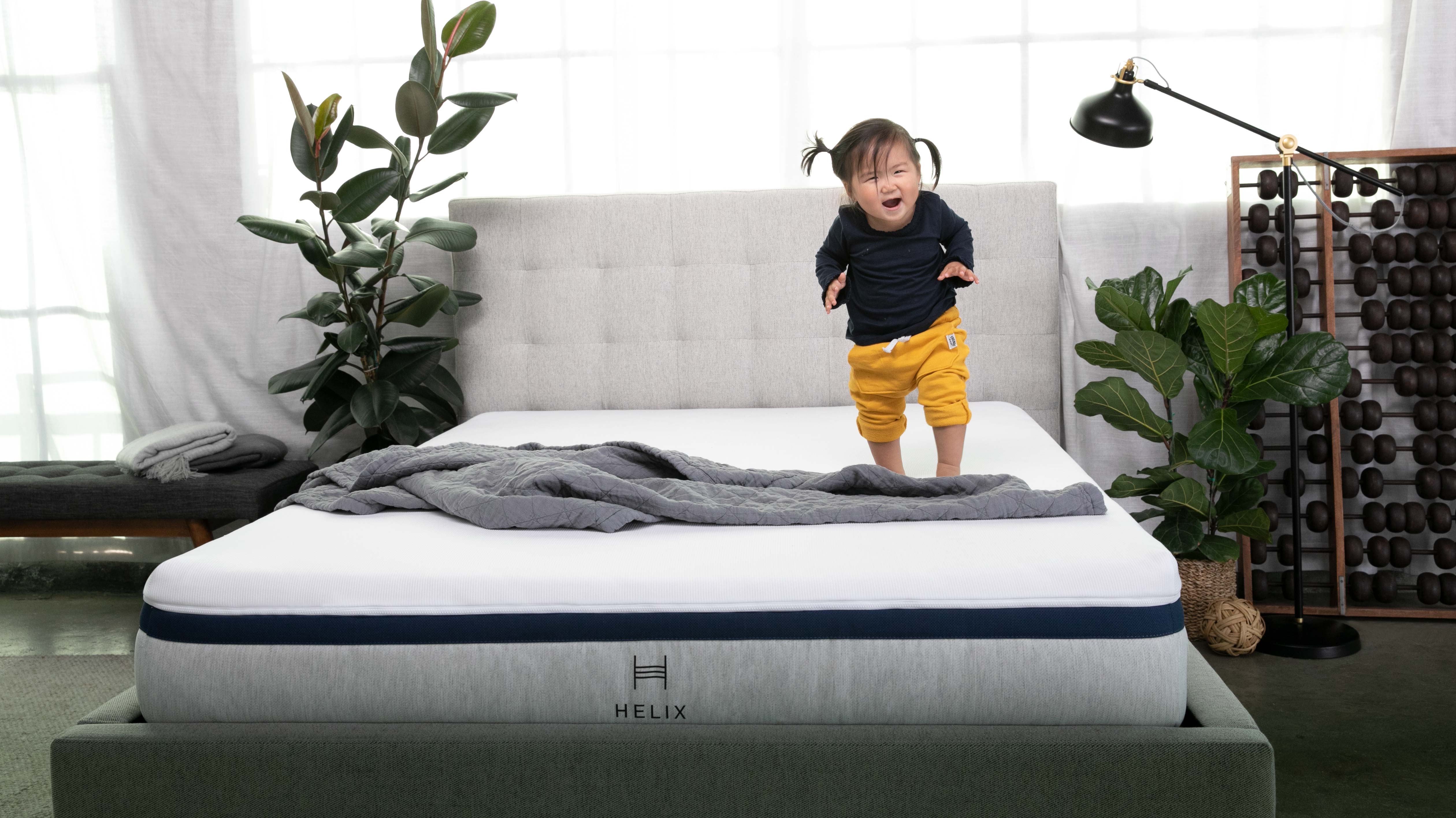 Helix Midnight mattress review: a toddler wearing a blue jumper and yellow trousers jumps on the Helix midnight mattress