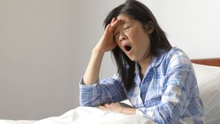 A woman sitting in bed, yawning widely