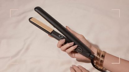 a womans hand holding the ghd original IV hair straightener against a pink backdrop