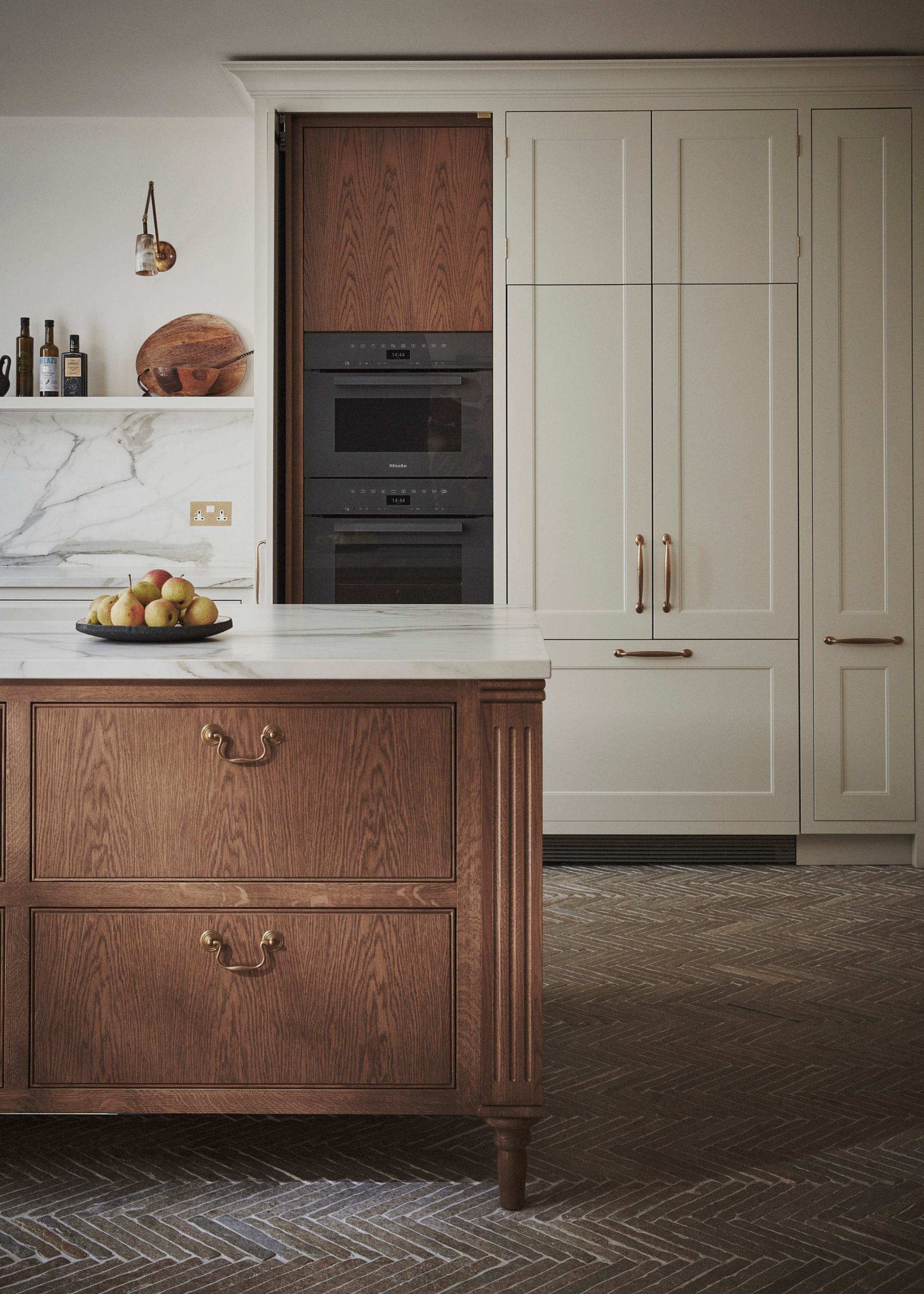 A modern kitchen with off-white built-in cabinetry, marble countertops and a freestanding wooden kitchen island with drawers, gold handles and a marble countertop