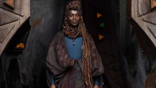 Jodie Turner-Smith stands smiling in front of a doorway, dressed in an ornate costume in The Acolyte.