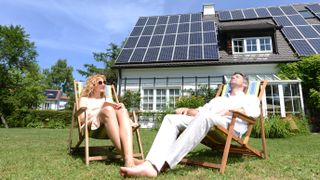 A couple sitting in deck chairs outside their home with solar panels on the roof