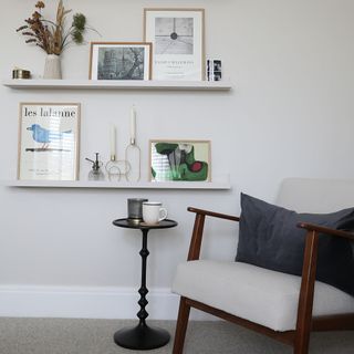 White painted room with mid-century armchair and shelving with framed artwork and decor