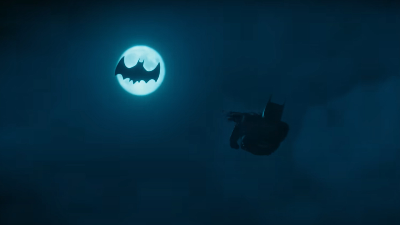 Batman dives down from the Batwing, which is silhouetted against the moon, in The Flash film