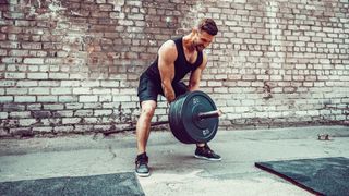 Man lifting a barbell with plates on using both hands during outdoor strength training session