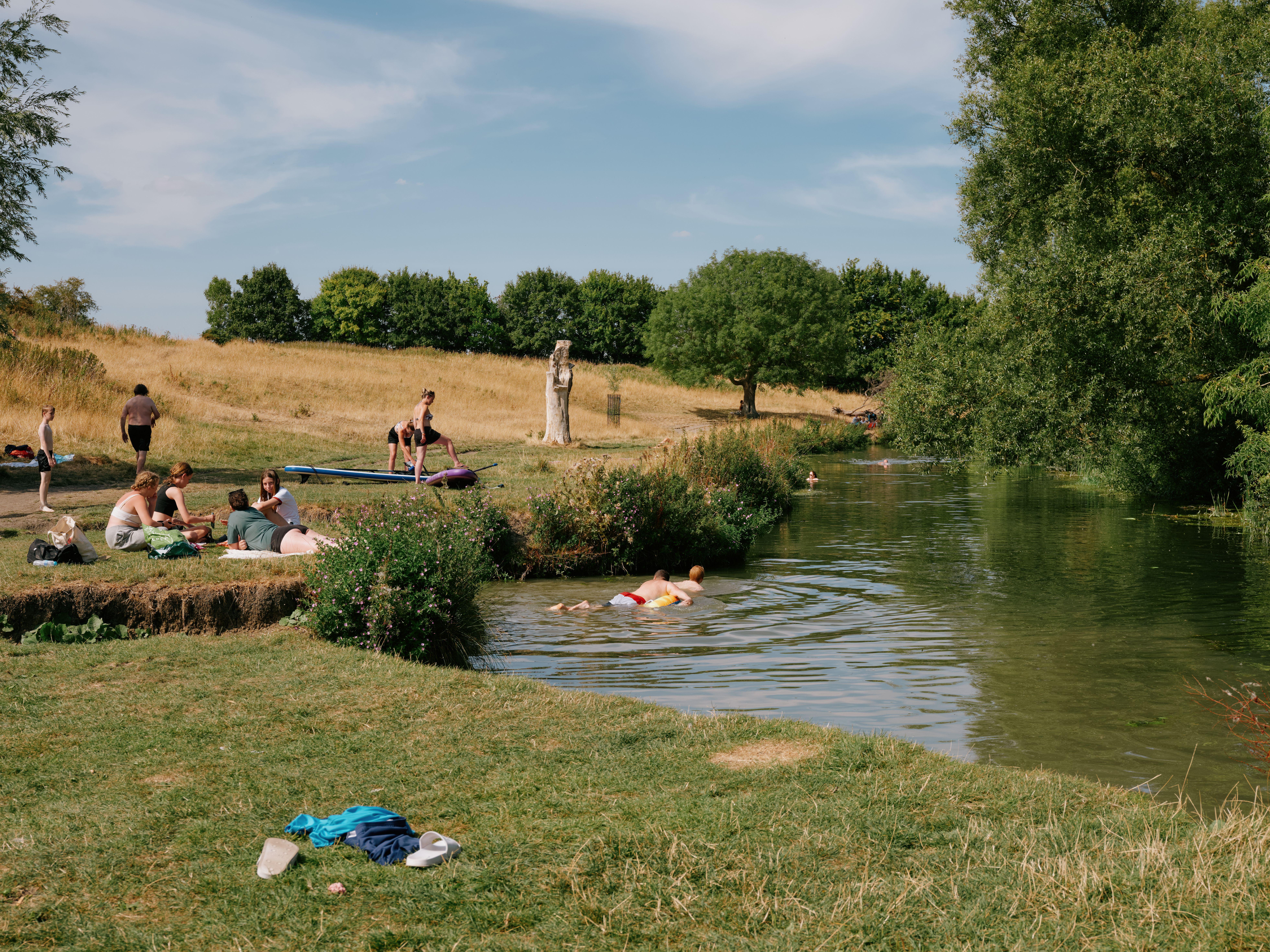 People swimming in and sitting next to the river in Grantchester Meadows