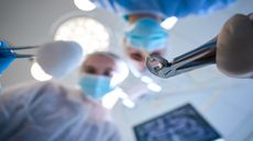 Dental surgeon standing over a person holding a tooth that has been extracted using forceps while another dentist stands next to them